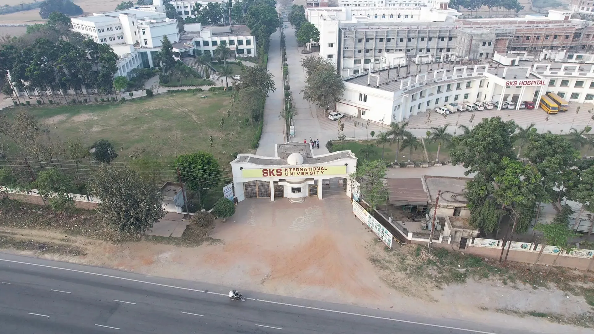Wide aerial view of the SKS International University entrance gate, academic block, and hospital